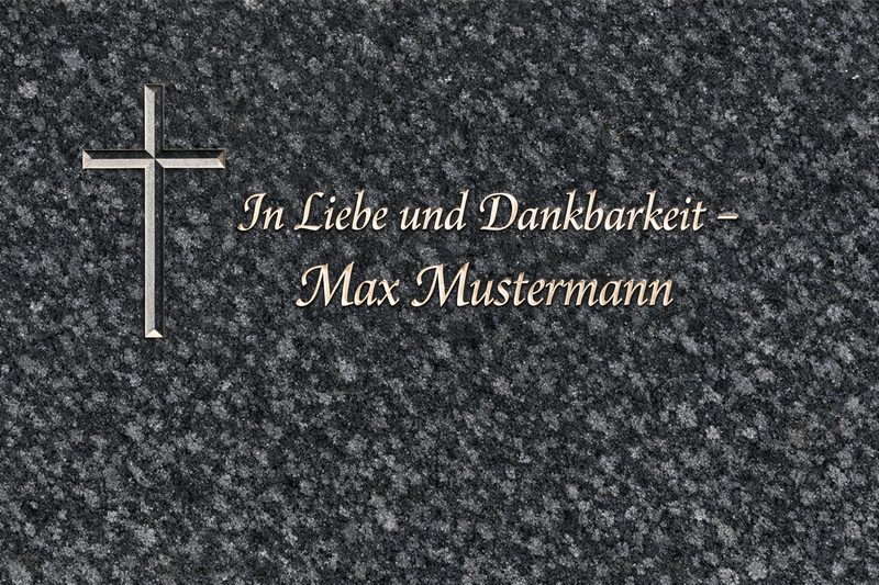 Impala‑Granit mit Keilnut‑Schriftzug 'In Liebe und Dankbarkeit – Max Mustermann' und Kreuz – harmonisch angeordnet im dunklen Naturstein